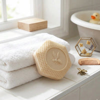 Hexagonal handcrafted oatmeal soap bar from the BaBee Nourish Collection for sensitive skin, featuring an embossed bee and honeycomb pattern propped against folded white towels.