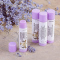 Four purple tubes of Texas Bee lip salve arranged on a textured stone surface. In the foreground, one tube stands uncapped to display a smooth, light purple Lavender Lemonade Propolis & Beeswax Lip Salve. Behind it, three additional tubes stand together, showcasing the vintage-style label details and ingredients. 