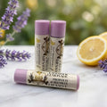 Three tubes of Lavender Lemonade Propolis & Beeswax Lip Salve with purple caps, displayed with fresh lavender and a lemon slice in the background.