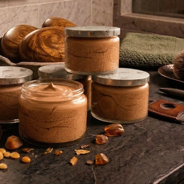 Jars of creamy Oakmoss & Amber men's body butter on a dark stone vanity.